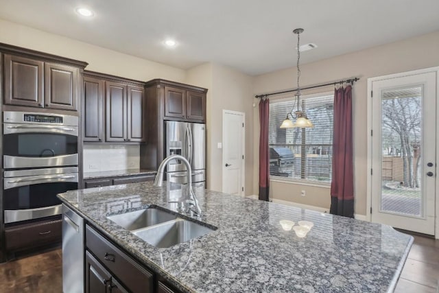 kitchen with sink, decorative light fixtures, dark brown cabinets, a center island with sink, and stainless steel appliances