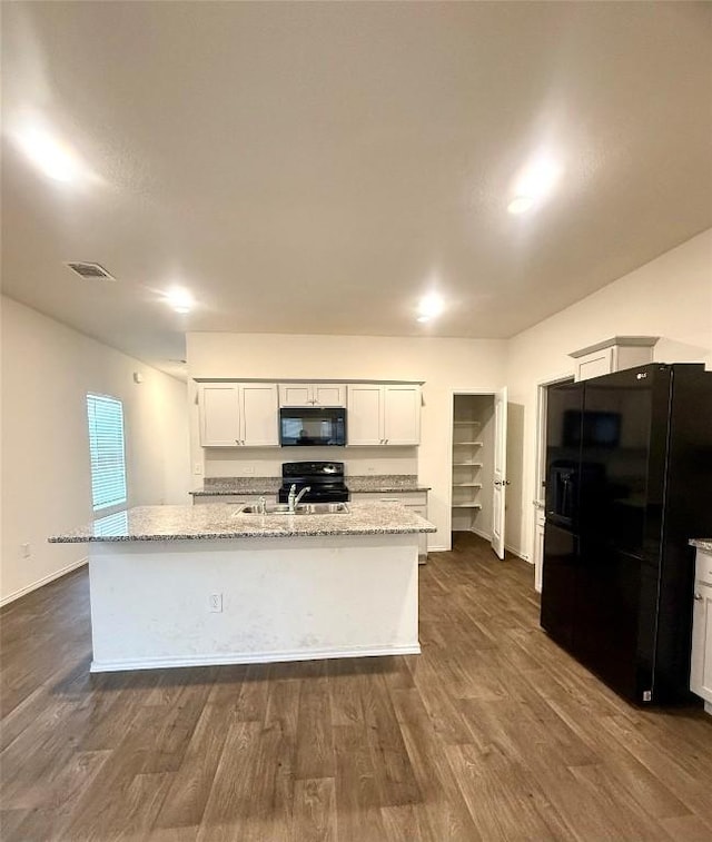 kitchen with light stone counters, white cabinets, an island with sink, and black appliances