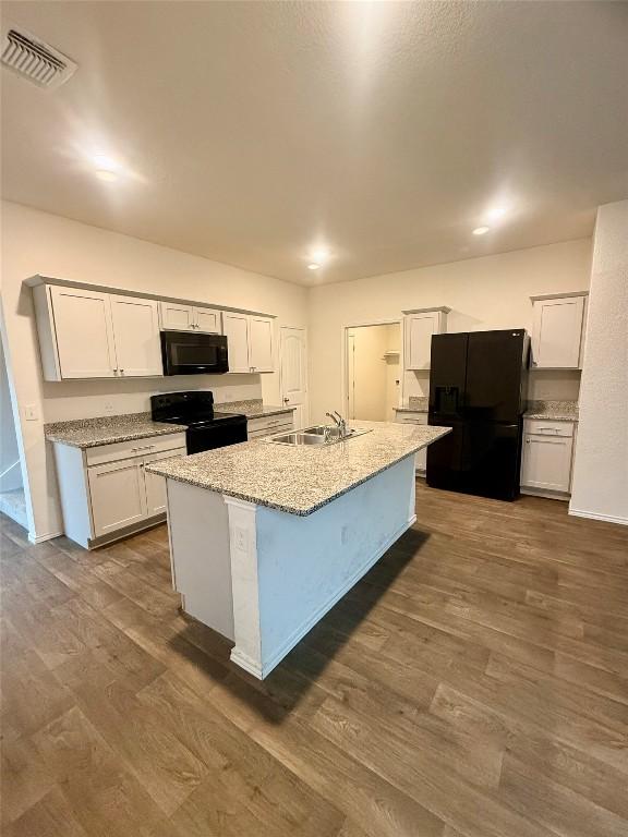 kitchen with white cabinetry, sink, black appliances, light stone countertops, and a center island with sink