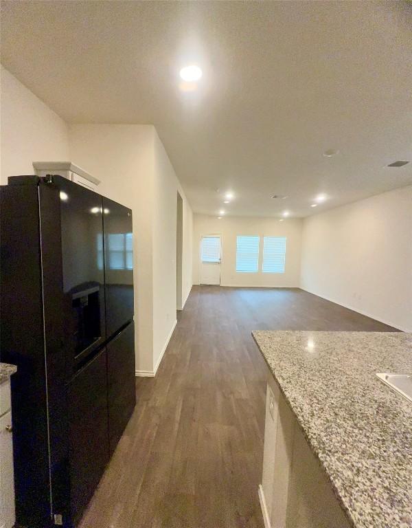 kitchen featuring light stone counters, dark hardwood / wood-style flooring, and black fridge