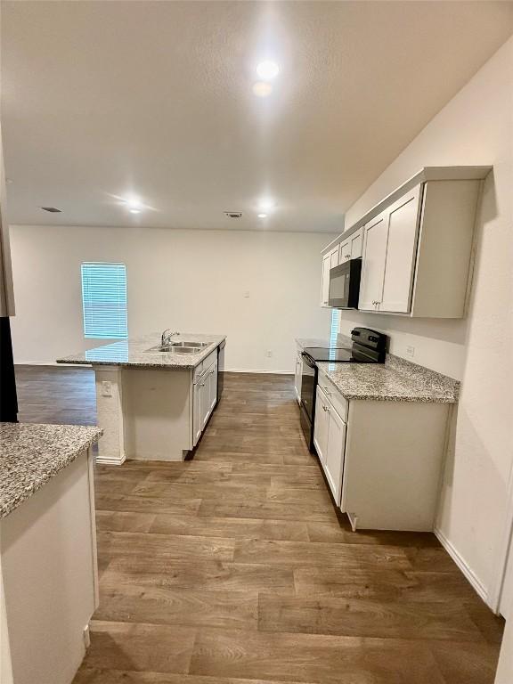 kitchen with light stone counters, an island with sink, hardwood / wood-style floors, and black appliances