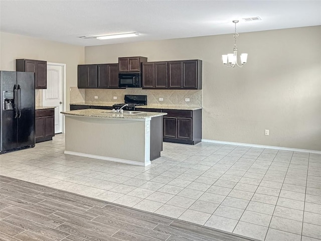 kitchen with a notable chandelier, an island with sink, backsplash, and black appliances