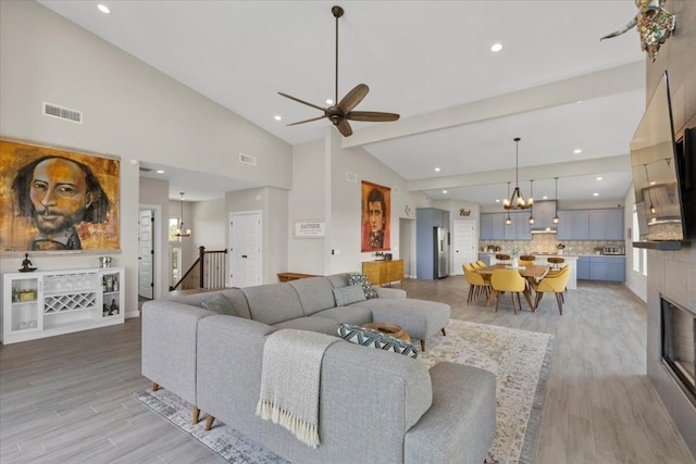 living room featuring high vaulted ceiling, ceiling fan with notable chandelier, and light wood-type flooring