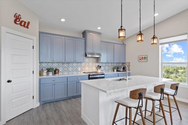 kitchen with pendant lighting, sink, electric stove, light stone countertops, and a center island with sink