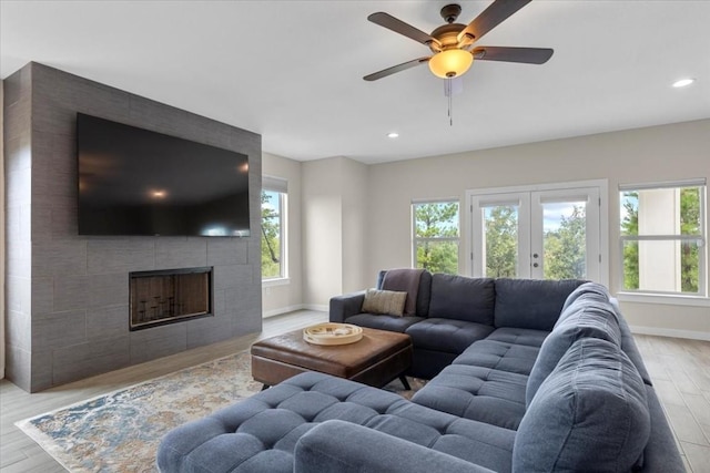 living room featuring a tiled fireplace, light hardwood / wood-style flooring, french doors, and ceiling fan