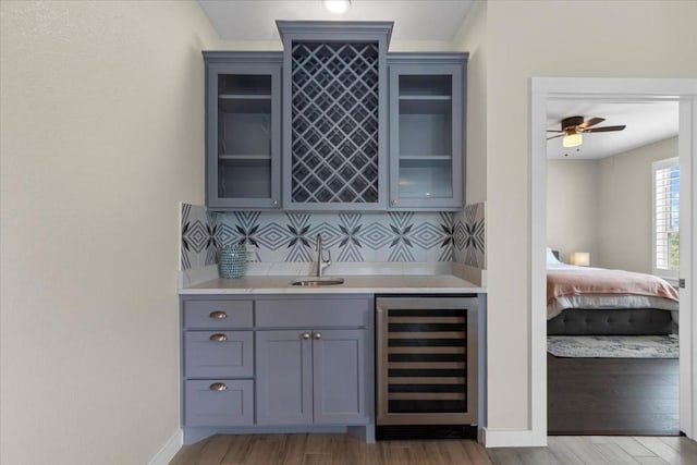 bar with wine cooler, sink, tasteful backsplash, ceiling fan, and light hardwood / wood-style floors