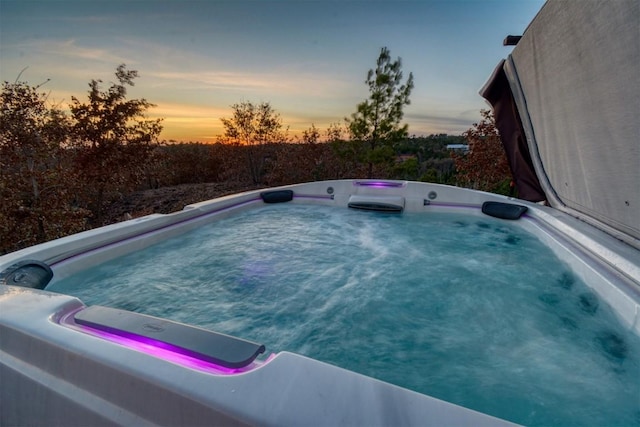 pool at dusk featuring a hot tub