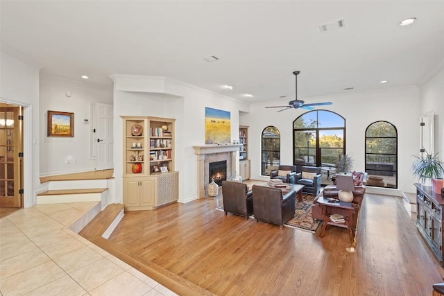 living room with built in shelves, ceiling fan, crown molding, and light hardwood / wood-style flooring