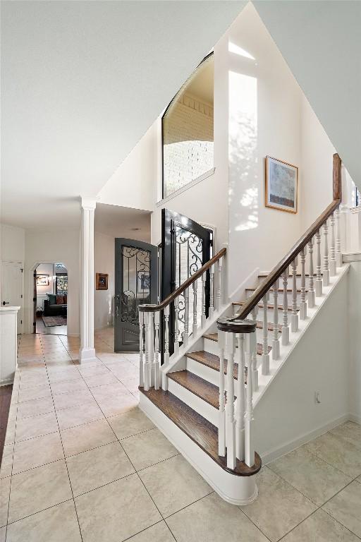 stairs featuring tile patterned floors, decorative columns, and a high ceiling