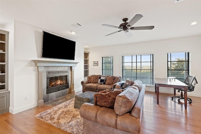 living room featuring ceiling fan, a fireplace, built in features, and light hardwood / wood-style flooring