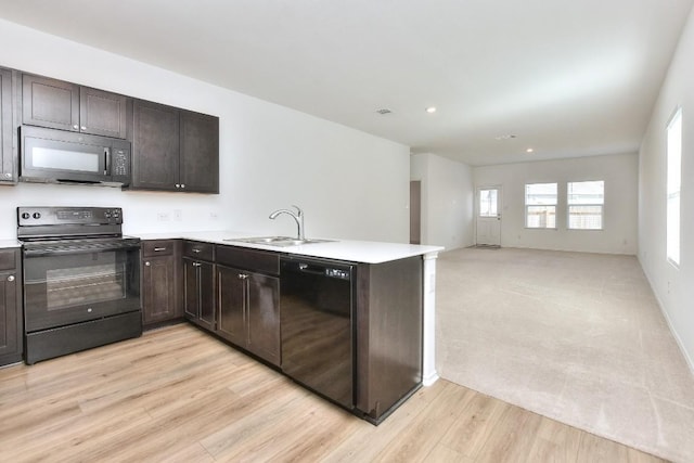 kitchen with dark brown cabinetry, a peninsula, a sink, light countertops, and black appliances