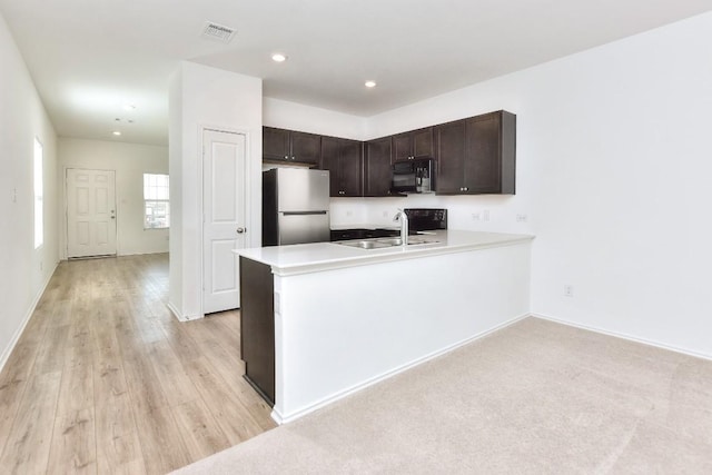 kitchen with visible vents, freestanding refrigerator, dark brown cabinetry, a sink, and black microwave