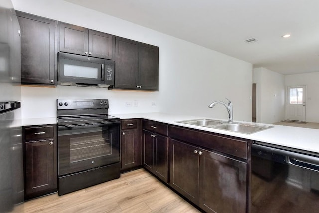 kitchen featuring light wood-style flooring, dark brown cabinetry, a sink, light countertops, and black appliances