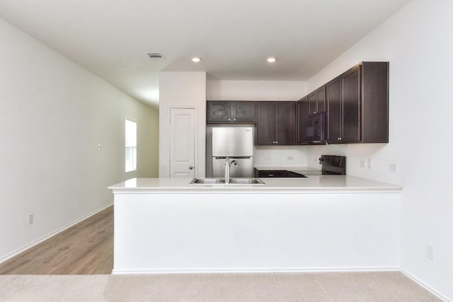 kitchen featuring a peninsula, a sink, dark brown cabinets, light countertops, and black appliances