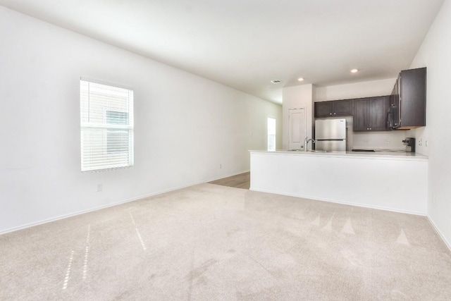 unfurnished living room with baseboards, light colored carpet, a sink, and recessed lighting