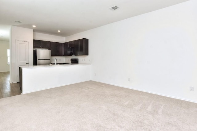 kitchen featuring black microwave, a peninsula, visible vents, and freestanding refrigerator