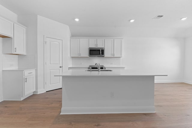 kitchen with a kitchen island with sink, sink, white cabinetry, and light hardwood / wood-style flooring