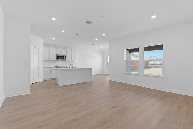 kitchen with sink, light hardwood / wood-style floors, a kitchen island with sink, and white cabinets