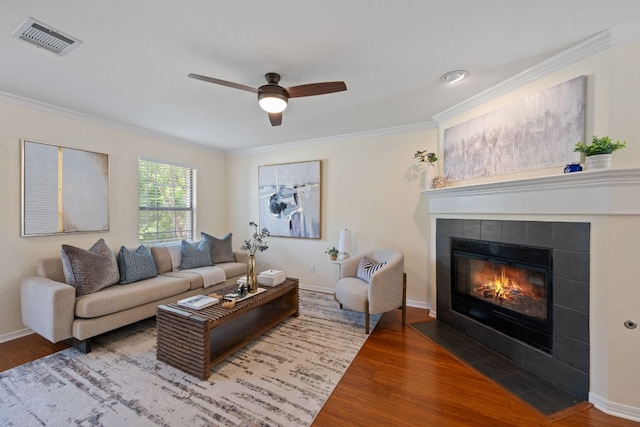 living room with visible vents, crown molding, wood finished floors, a fireplace, and a ceiling fan