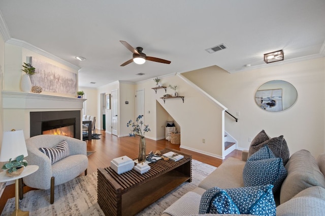 living area with visible vents, ornamental molding, wood finished floors, stairway, and a tiled fireplace