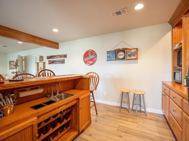 interior space with beam ceiling, sink, and light hardwood / wood-style floors