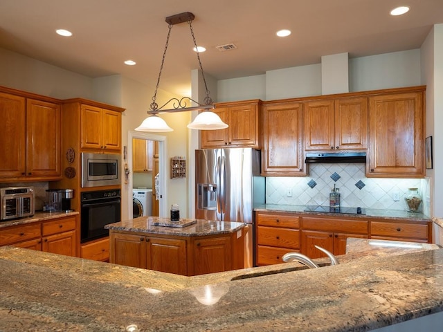 kitchen featuring stone countertops, hanging light fixtures, a center island with sink, and black appliances