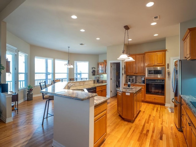 kitchen with hanging light fixtures, a spacious island, light stone counters, black appliances, and a kitchen bar