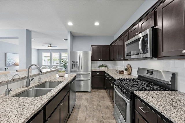 kitchen with sink, appliances with stainless steel finishes, backsplash, dark brown cabinetry, and light stone countertops