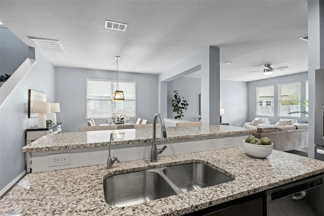 kitchen featuring hanging light fixtures, light stone countertops, sink, and stainless steel dishwasher