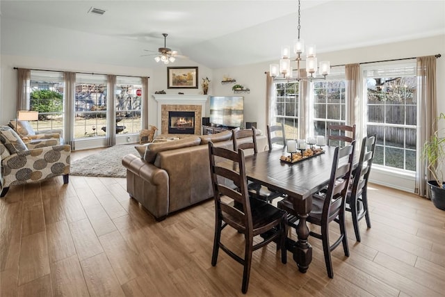 dining space with lofted ceiling, ceiling fan with notable chandelier, and light hardwood / wood-style flooring