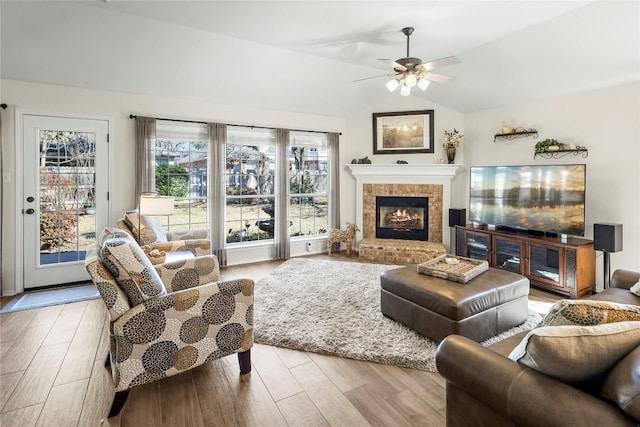 living room featuring a brick fireplace, vaulted ceiling, ceiling fan, and light wood-type flooring