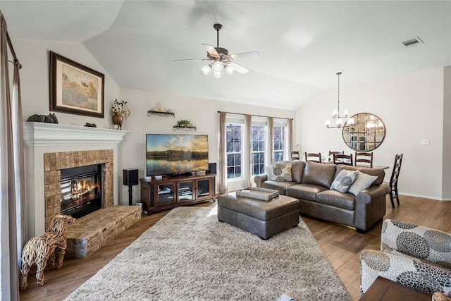 living room featuring vaulted ceiling, wood-type flooring, ceiling fan with notable chandelier, and a fireplace