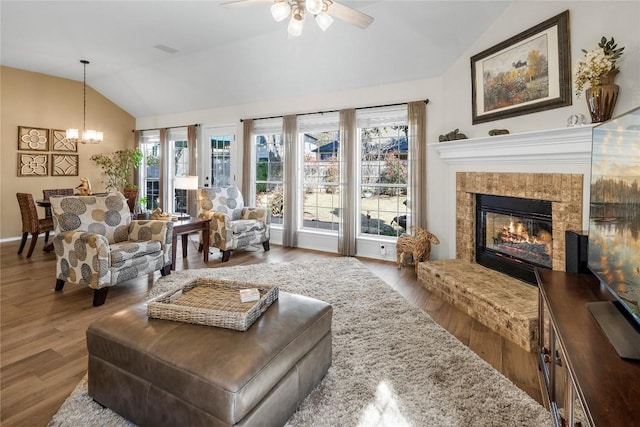 living room featuring vaulted ceiling, ceiling fan with notable chandelier, hardwood / wood-style floors, and a fireplace