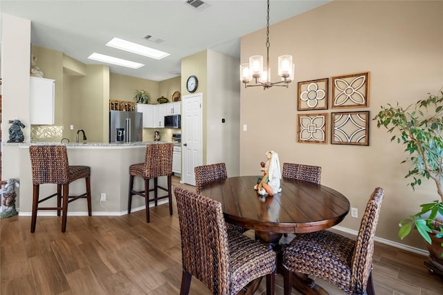 dining space with dark wood-type flooring, an inviting chandelier, and a skylight