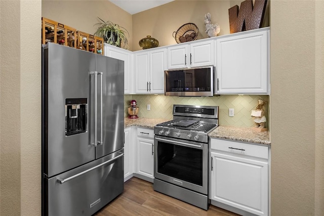 kitchen with stainless steel appliances, tasteful backsplash, light stone countertops, and white cabinets