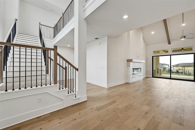 unfurnished living room featuring high vaulted ceiling, light hardwood / wood-style flooring, beamed ceiling, ceiling fan, and a tiled fireplace