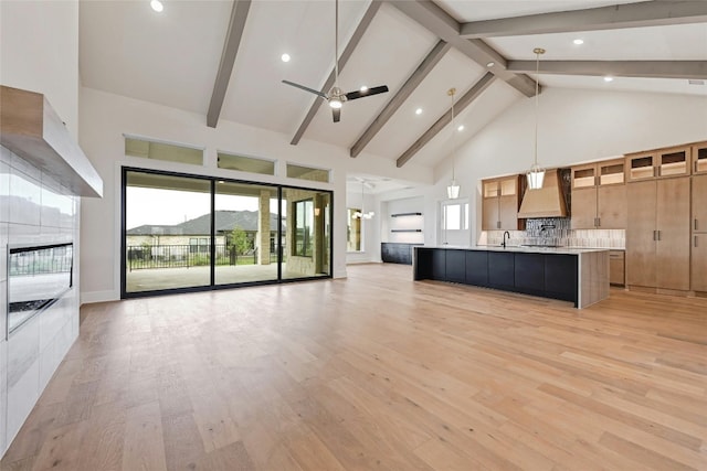 kitchen featuring high vaulted ceiling, a large island with sink, custom exhaust hood, hanging light fixtures, and light hardwood / wood-style floors