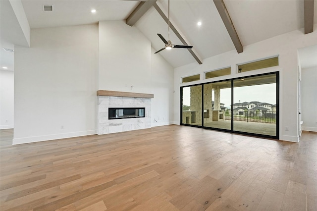 unfurnished living room featuring a stone fireplace, high vaulted ceiling, ceiling fan, beam ceiling, and light hardwood / wood-style flooring