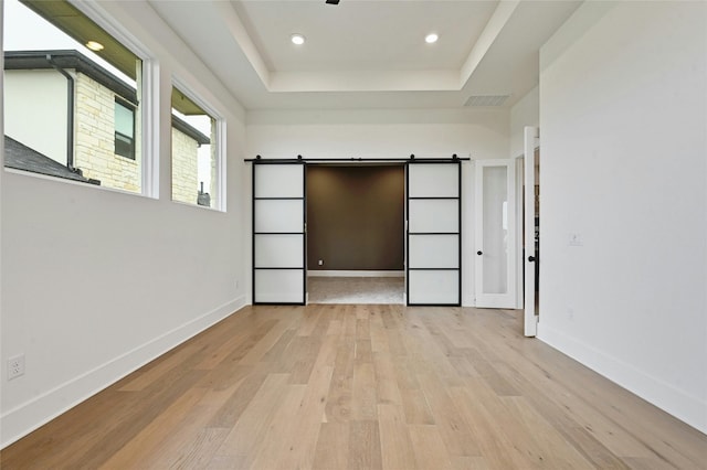 unfurnished bedroom with a barn door, a raised ceiling, and light hardwood / wood-style flooring