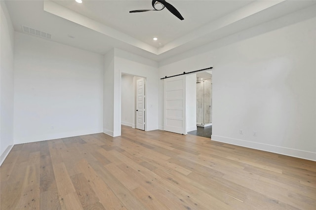 unfurnished bedroom featuring ceiling fan, a barn door, a raised ceiling, and light hardwood / wood-style floors