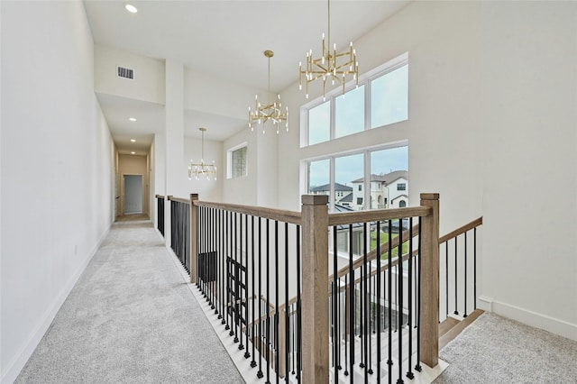 corridor with a high ceiling, light colored carpet, and an inviting chandelier