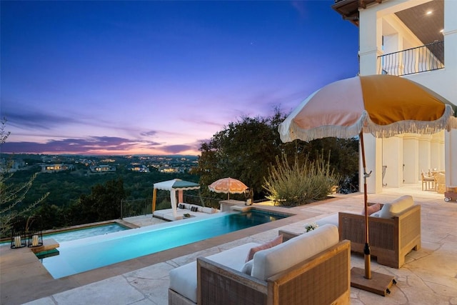 pool at dusk featuring a hot tub, an outdoor hangout area, and a patio