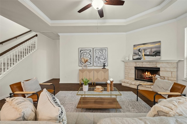 living room featuring ornamental molding, a stone fireplace, a raised ceiling, and hardwood / wood-style floors