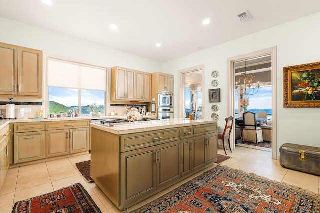 kitchen with a kitchen island, appliances with stainless steel finishes, light brown cabinetry, light tile patterned floors, and a notable chandelier