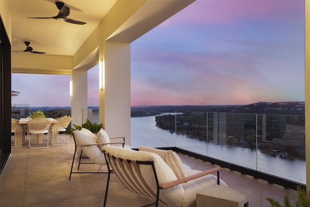 balcony at dusk featuring an outdoor living space, a patio area, ceiling fan, and a water view