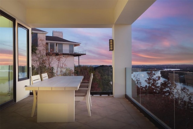 balcony at dusk featuring a water view and a patio area