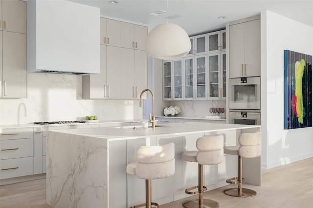 kitchen featuring stainless steel double oven, a breakfast bar, a kitchen island with sink, and backsplash