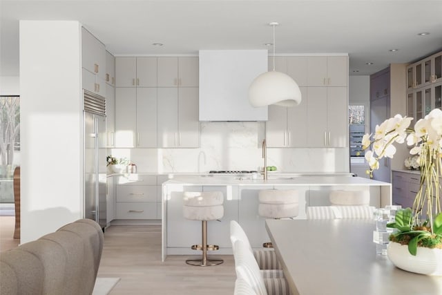 kitchen with sink, a breakfast bar, decorative backsplash, built in fridge, and light wood-type flooring