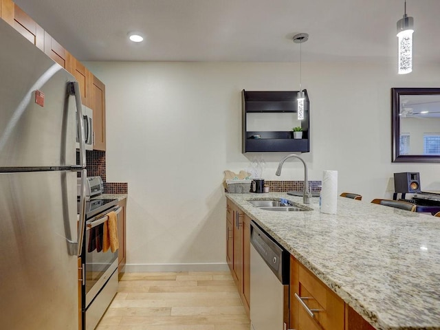 kitchen featuring appliances with stainless steel finishes, sink, pendant lighting, and light stone counters