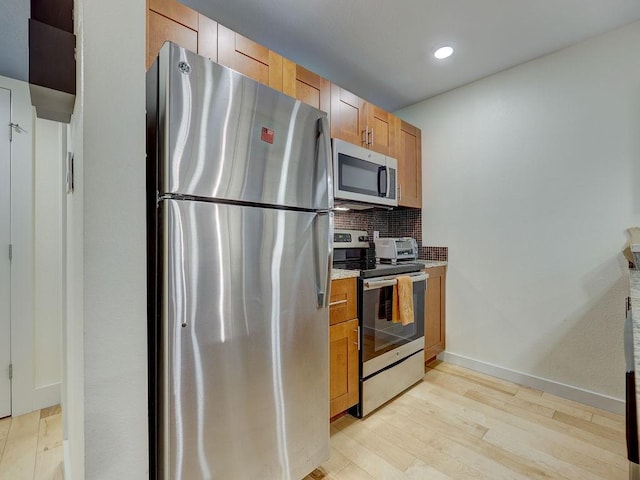 kitchen with appliances with stainless steel finishes, light hardwood / wood-style floors, and backsplash